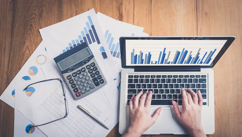 Overhead view of a laptop showing financial charts beside paperwork and a calculator