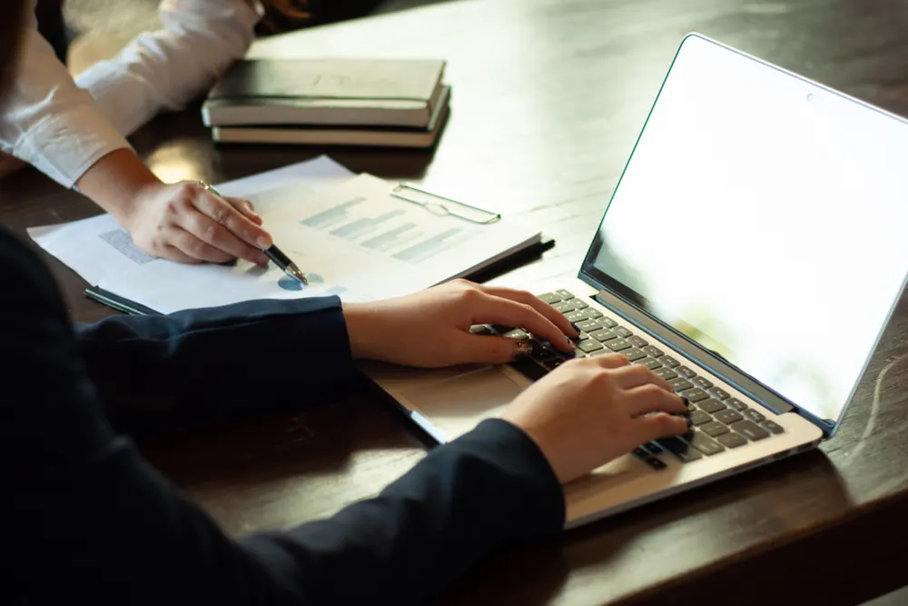 Two business owners reviewing financial documents together, one on a laptop
